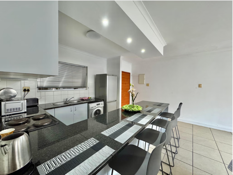 Open-plan kitchen featuring granite countertops, a breakfast bar, integrated appliances, and tiled flooring, seamlessly flowing into the living area.