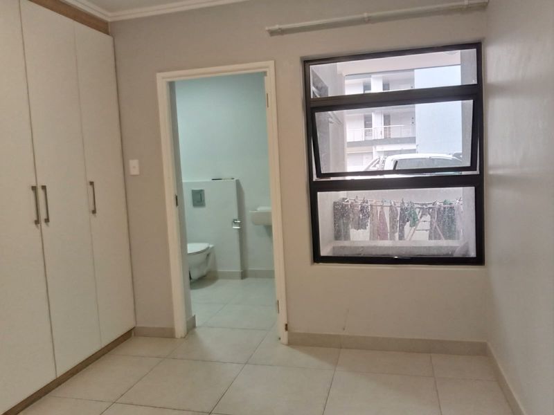 A clean, empty bedroom featuring built-in cupboards, tiled flooring, and an adjoining en-suite bathroom with modern fixtures.
