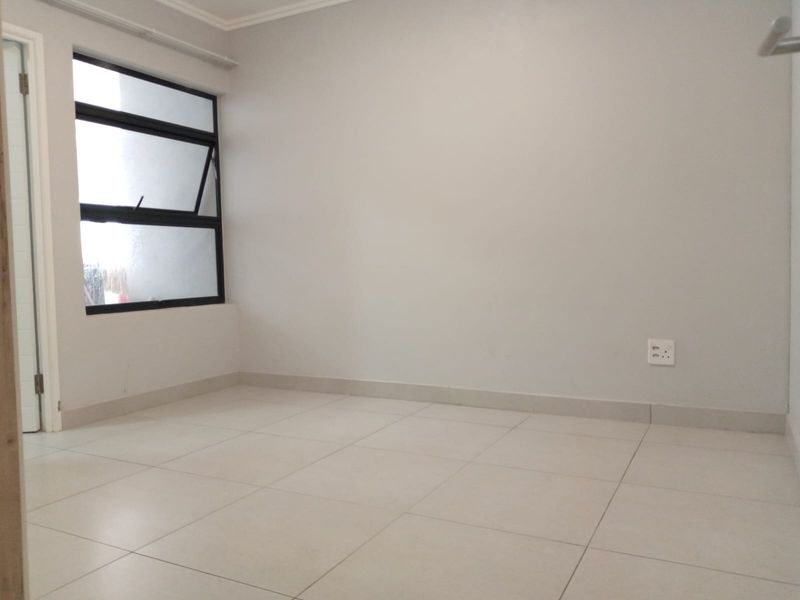 A clean, empty bedroom featuring neutral tiled flooring and a modern aluminium-framed window, providing a blank canvas for interior design.