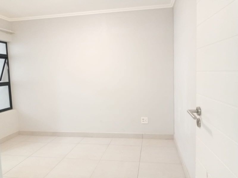 A clean, empty bedroom featuring neutral tiled flooring, white walls, and an aluminium-framed window, providing a blank canvas for interior design.