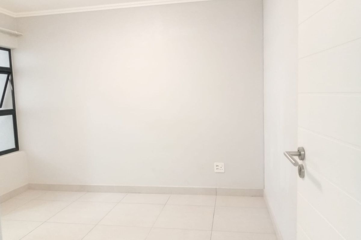A clean, empty bedroom featuring neutral tiled flooring, white walls, and an aluminium-framed window, providing a blank canvas for interior design.