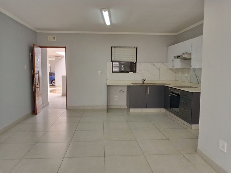 Modern open-plan kitchen featuring sleek grey and white cabinetry, built-in oven, extractor fan, and marble-look splashback, set against neutral tiled flooring.