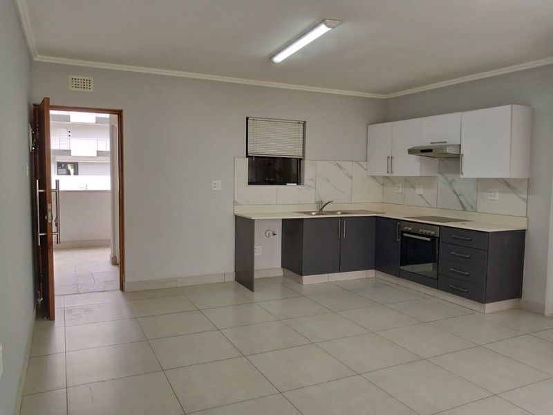 A clean, modern kitchen featuring dark lower cabinets, white upper cabinets, marble-look splashbacks, and integrated appliances, with tiled flooring throughout.