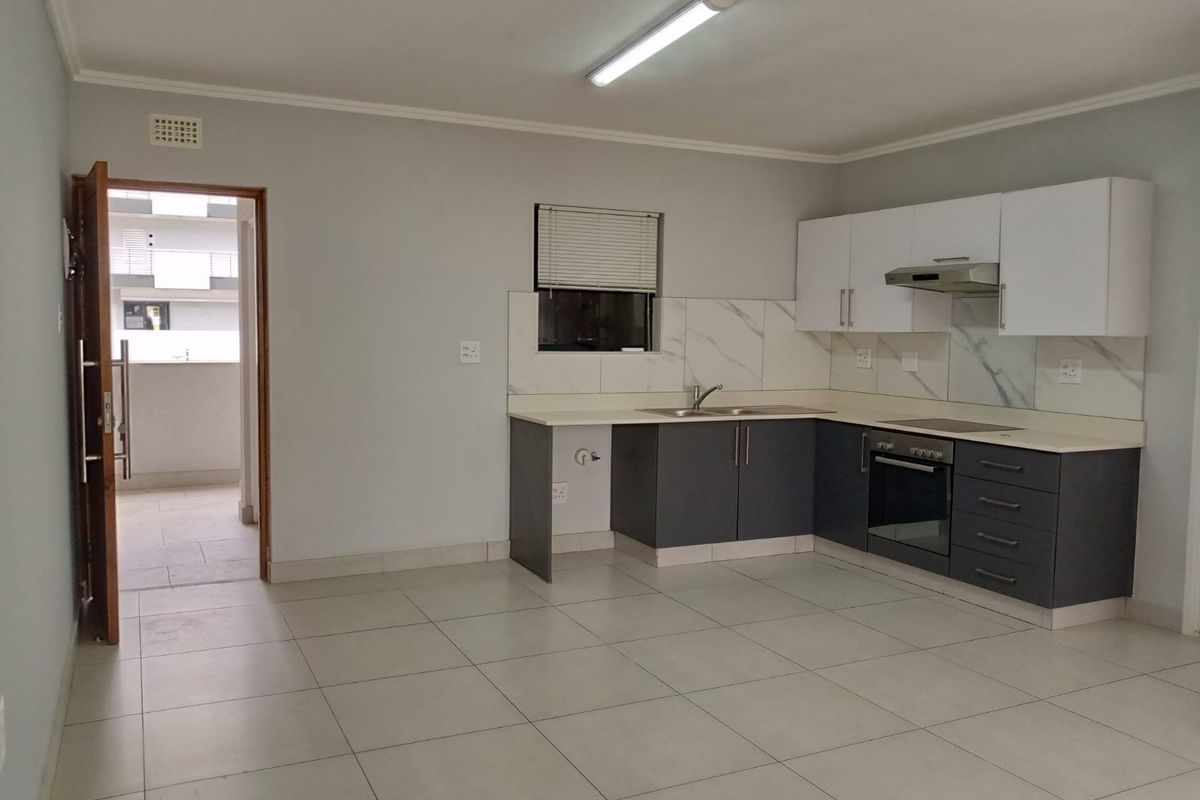 A clean, modern kitchen featuring dark lower cabinets, white upper cabinets, marble-look splashbacks, and integrated appliances, with tiled flooring throughout.
