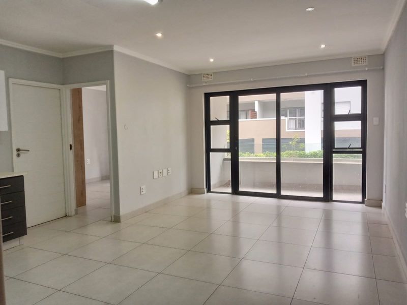 Bright open-plan living area featuring neutral tiled flooring, recessed lighting, and large sliding glass doors providing access to the balcony.