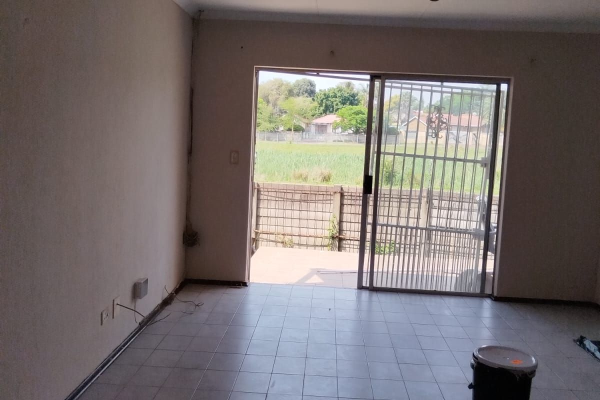 An empty living room featuring tiled flooring, a sliding glass door with a security gate, and access to an outdoor area.