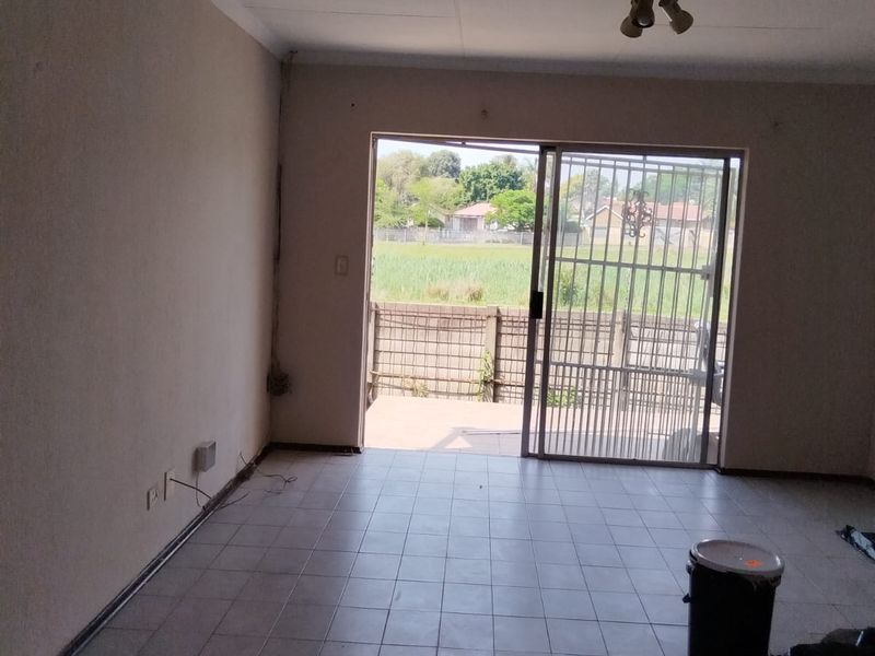 An empty living room featuring tiled flooring, a sliding glass door with a security gate, and access to an outdoor area.
