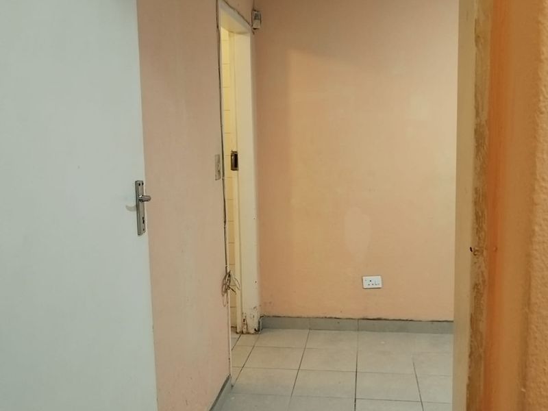 An empty hallway featuring tiled flooring and peach-toned walls, showing signs of wear and requiring minor cosmetic updates.