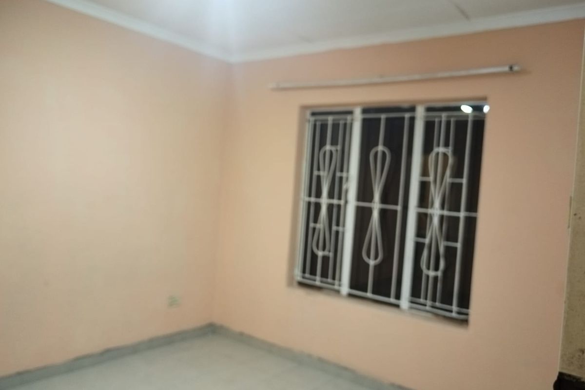 An empty bedroom featuring tiled flooring, peach-toned walls, and a window fitted with white security bars.