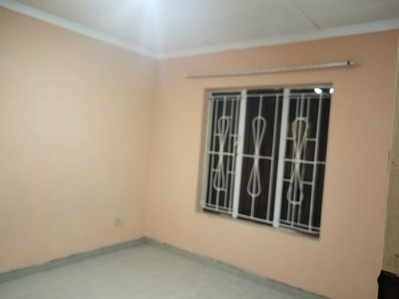 An empty bedroom featuring tiled flooring, peach-toned walls, and a window fitted with white security bars.