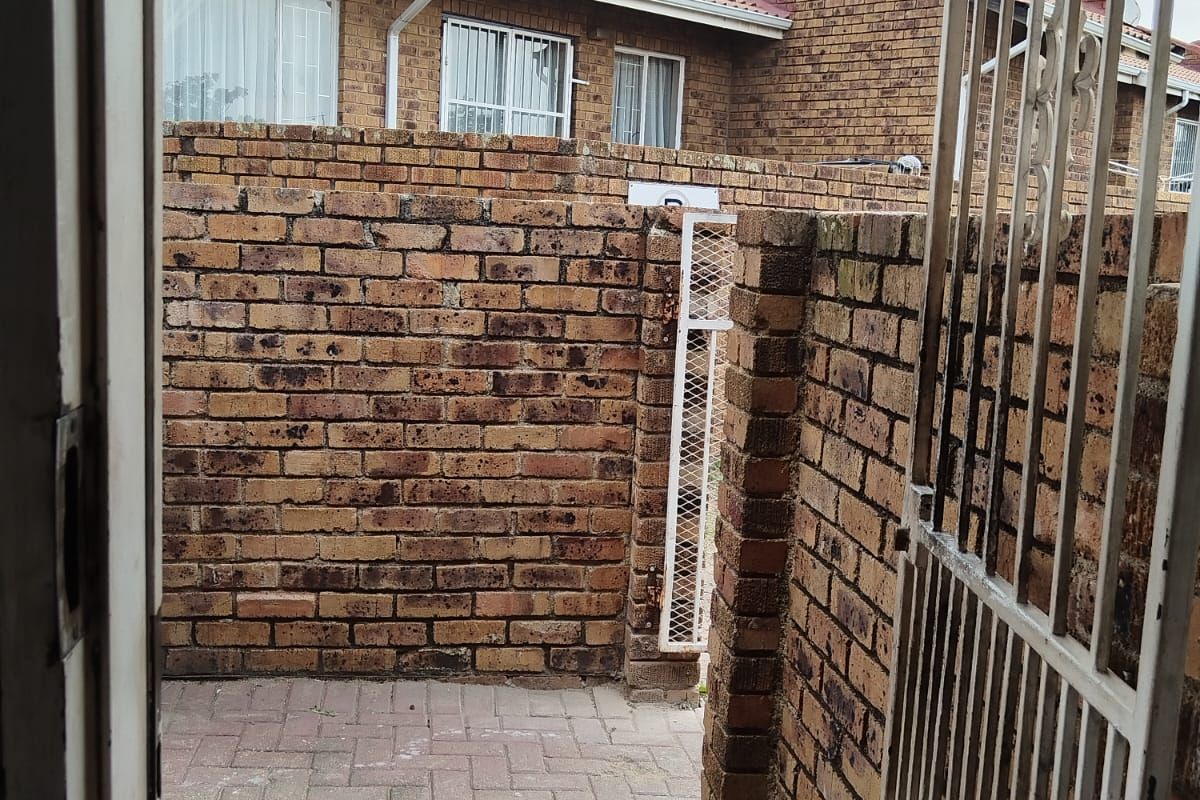 A private rear courtyard featuring brick boundary walls, paved flooring, and a secure metal gate, providing a functional outdoor space.