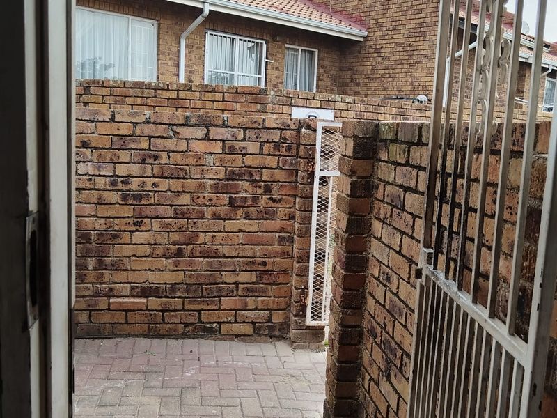 A private rear courtyard featuring brick boundary walls, paved flooring, and a secure metal gate, providing a functional outdoor space.
