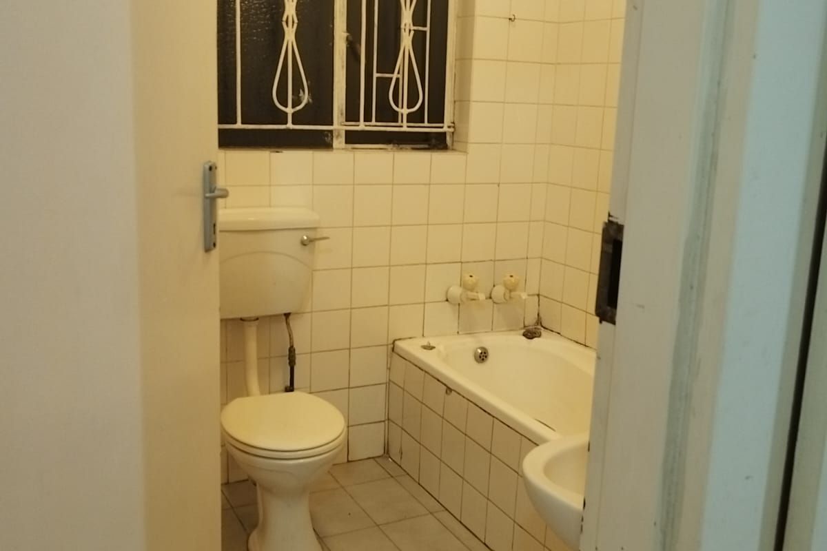 A dated bathroom featuring a built-in bathtub, pedestal basin, and toilet, finished with white ceramic wall and floor tiles.