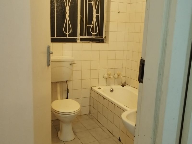 A dated bathroom featuring a built-in bathtub, pedestal basin, and toilet, finished with white ceramic wall and floor tiles.