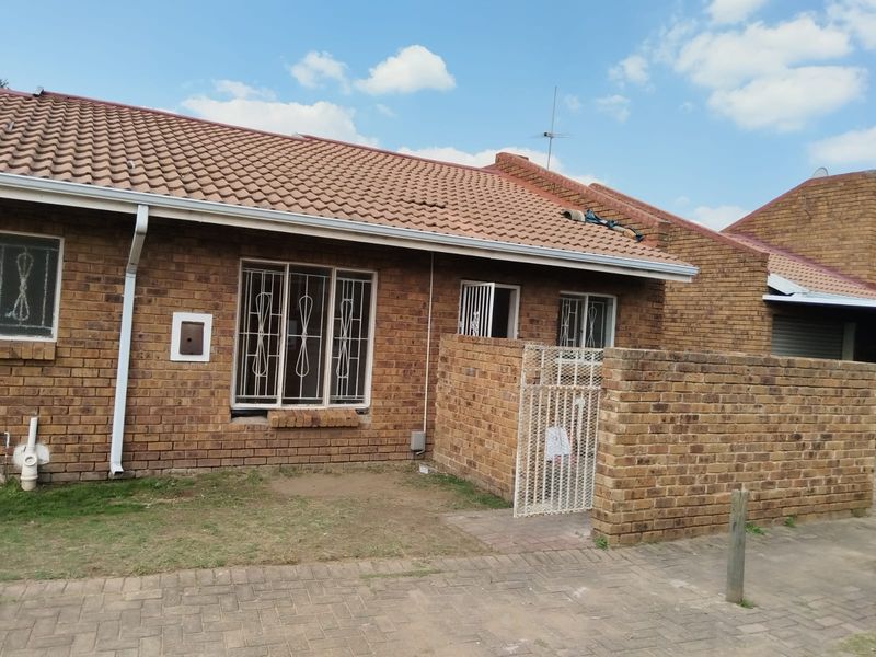 Front exterior view of a face brick apartment unit featuring a tiled roof, security bars on windows, and a private brick-walled entrance area.