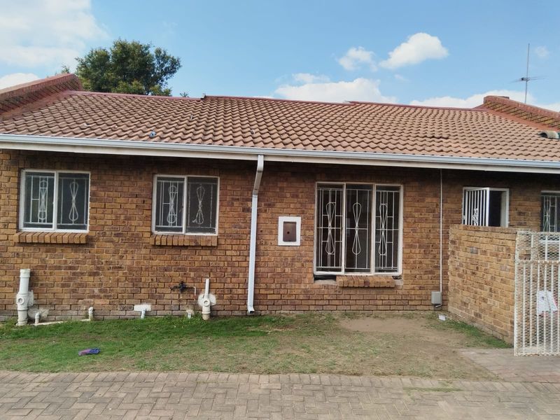 Front elevation of a face brick apartment unit featuring a tiled roof, security bars on windows, and external plumbing fixtures.