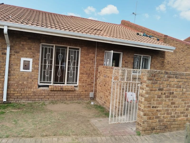 Exterior view of a face brick apartment unit featuring a tiled roof, security bars on windows, and a small private courtyard area.