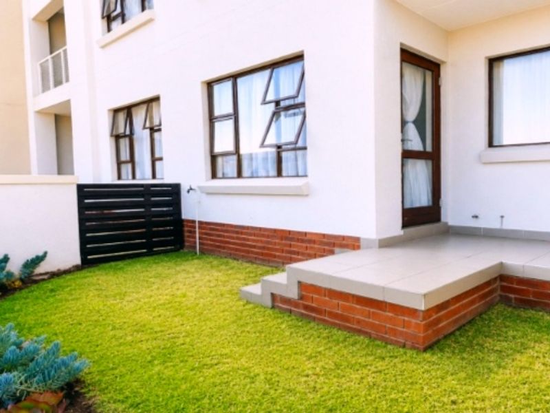 A well-maintained rear exterior view featuring a tiled patio, brick foundation, and a private garden area with established landscaping.