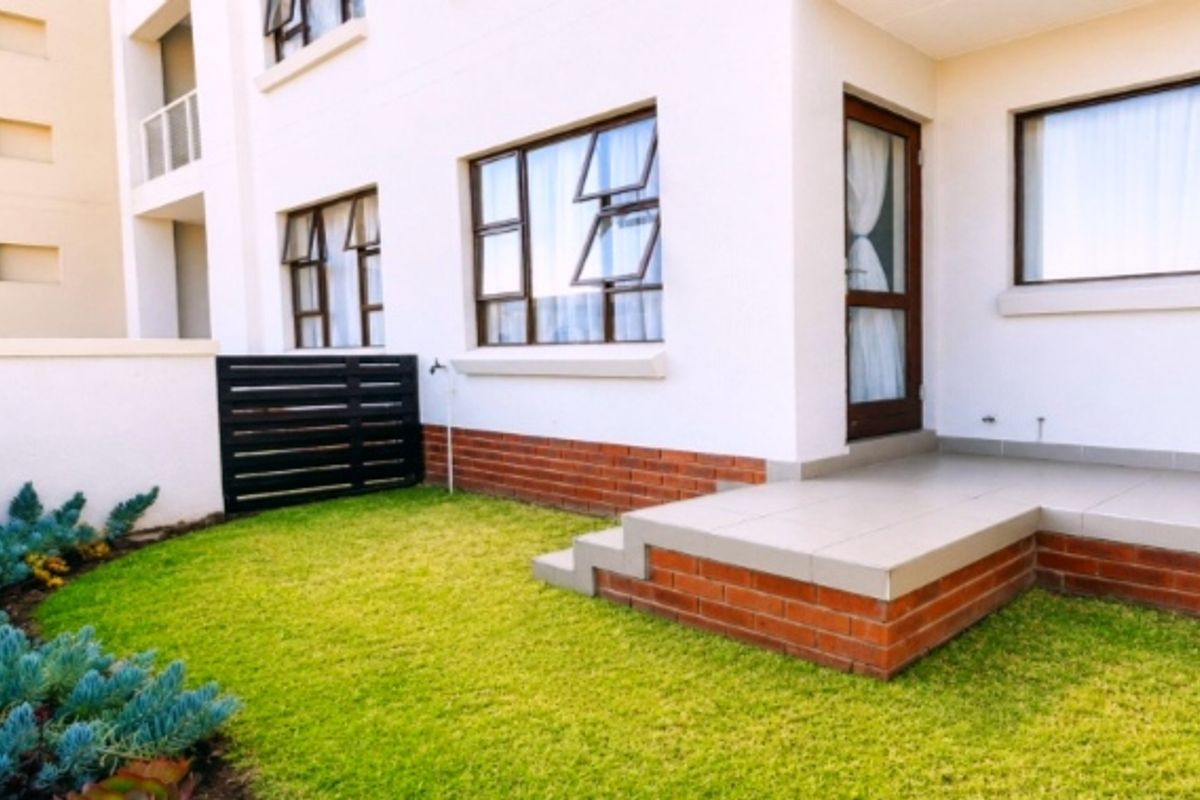 A well-maintained rear exterior view featuring a tiled patio, brick foundation, and a private garden area with established landscaping.