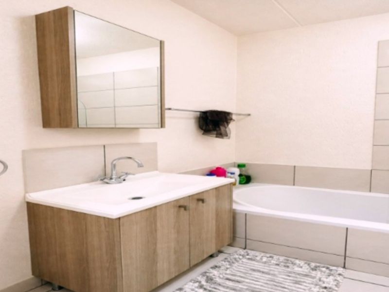 A functional bathroom featuring a wood-finish vanity with integrated basin, mirrored cabinet, and a tiled bathtub area.