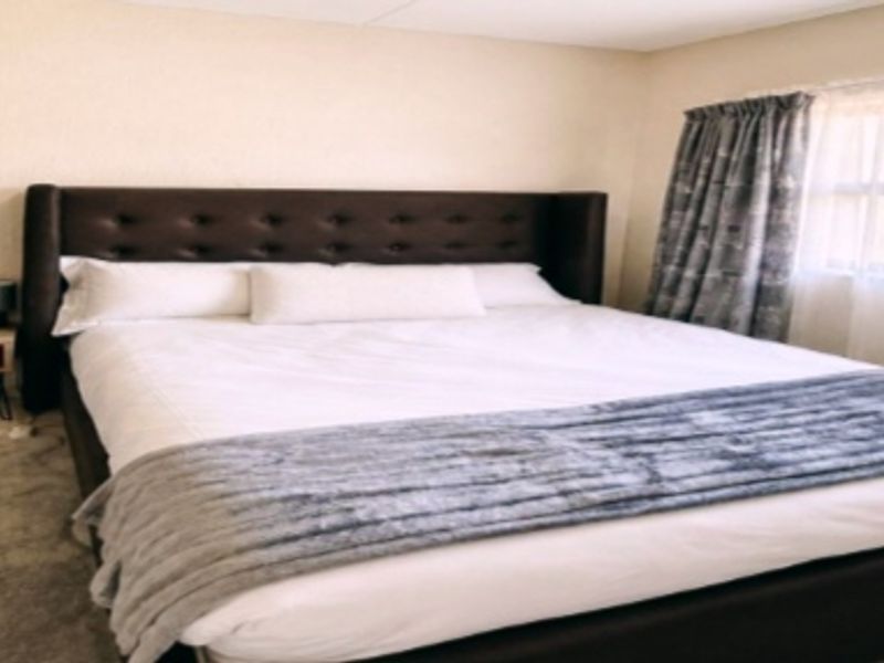 A well-lit bedroom featuring a built-in wardrobe, tiled flooring, and a large window with curtains, providing a comfortable and functional living space.