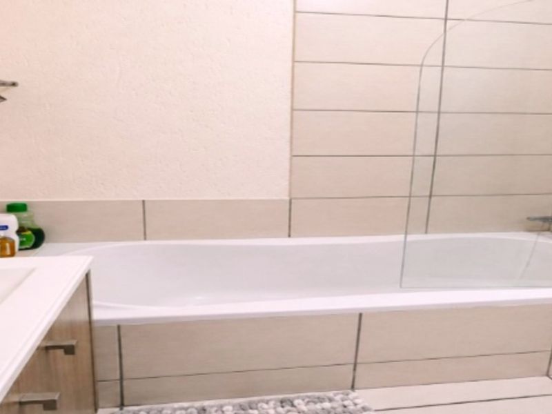 A functional bathroom featuring a bathtub with a glass shower screen, tiled walls, and a vanity cabinet.