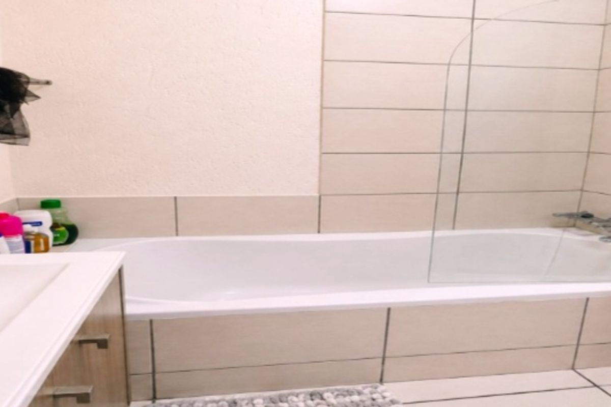 A functional bathroom featuring a bathtub with a glass shower screen, tiled walls, and a vanity cabinet.