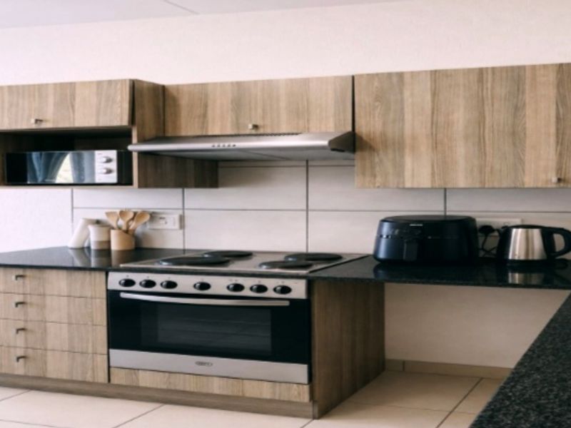 A functional kitchen featuring wood-look cabinetry, black granite countertops, a built-in oven with electric hob, and a tiled backsplash.