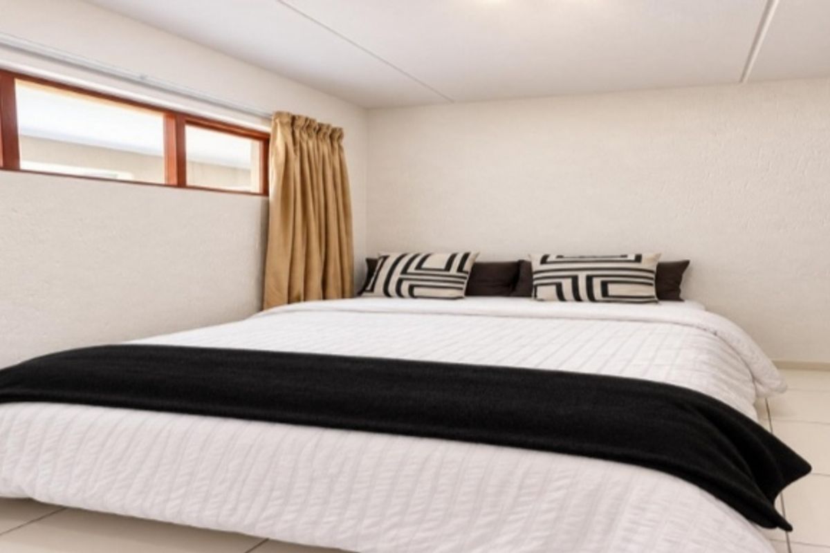 A bedroom featuring tiled flooring and timber-framed windows, providing a neutral and functional space.