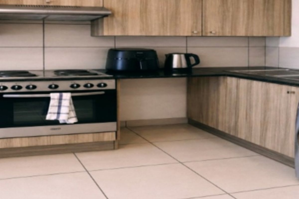 A functional kitchen featuring wood-look cabinetry, a built-in oven and hob, extractor fan, double sink, and tiled finishes with integrated laundry plumbing.