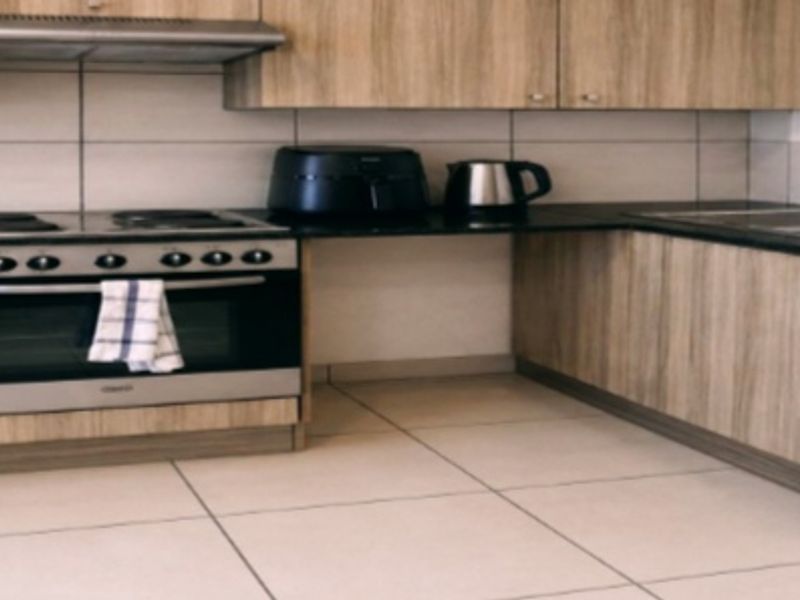 A functional kitchen featuring wood-look cabinetry, a built-in oven and hob, extractor fan, double sink, and tiled finishes with integrated laundry plumbing.