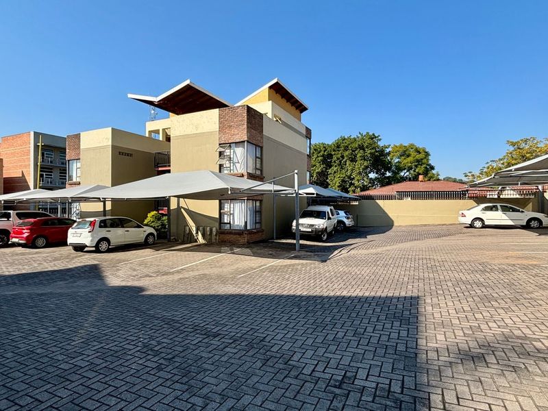 Exterior view of the apartment complex featuring a paved parking area with installed shade sail carports and brick building facade.