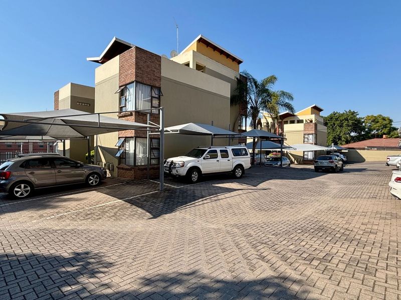 Exterior view of the apartment complex featuring a paved parking area with multiple covered carport bays and multi-story residential building architecture.