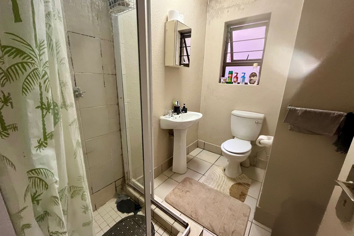 A compact bathroom featuring a pedestal basin, toilet, and shower enclosure. The space shows signs of wear and requires maintenance or renovation.