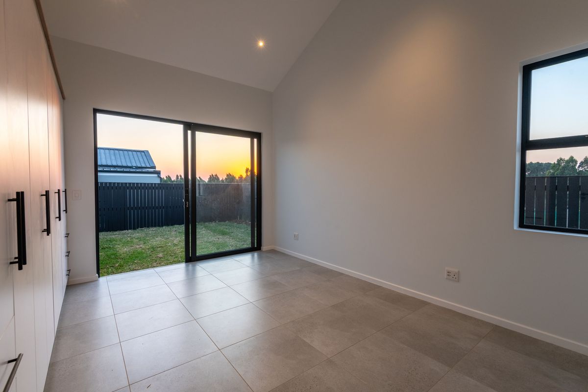 A bright, modern bedroom featuring vaulted ceilings, tiled flooring, built-in cupboards, and a sliding glass door providing direct access to the rear garden.