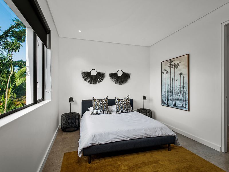 A modern, well-lit bedroom featuring tiled flooring, recessed downlighting, and a large window with garden views, including direct access to an en-suite bathroom.