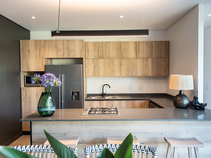 Modern kitchen featuring wood-grain cabinetry, stone countertops, a central gas cooktop, and integrated lighting, offering a sleek and functional culinary space.
