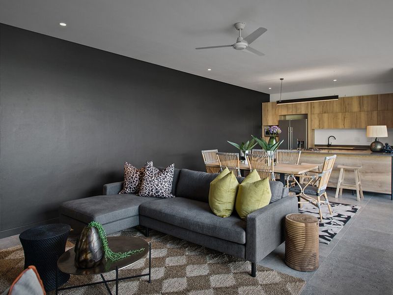 Modern open-plan living and dining area featuring a sleek kitchen with wood-finish cabinetry, recessed lighting, and large format floor tiles.