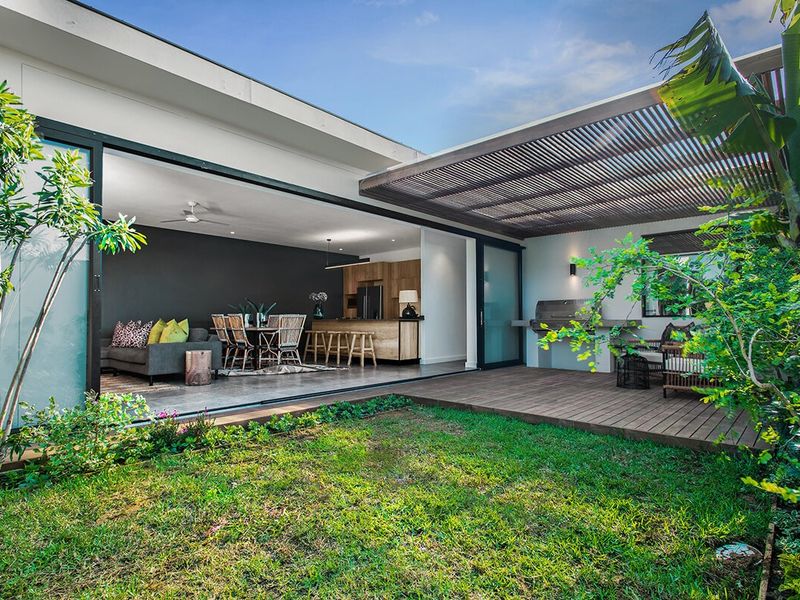 Modern covered patio featuring timber decking, a slatted pergola, and a built-in outdoor braai, seamlessly connecting to the open-plan interior living space.