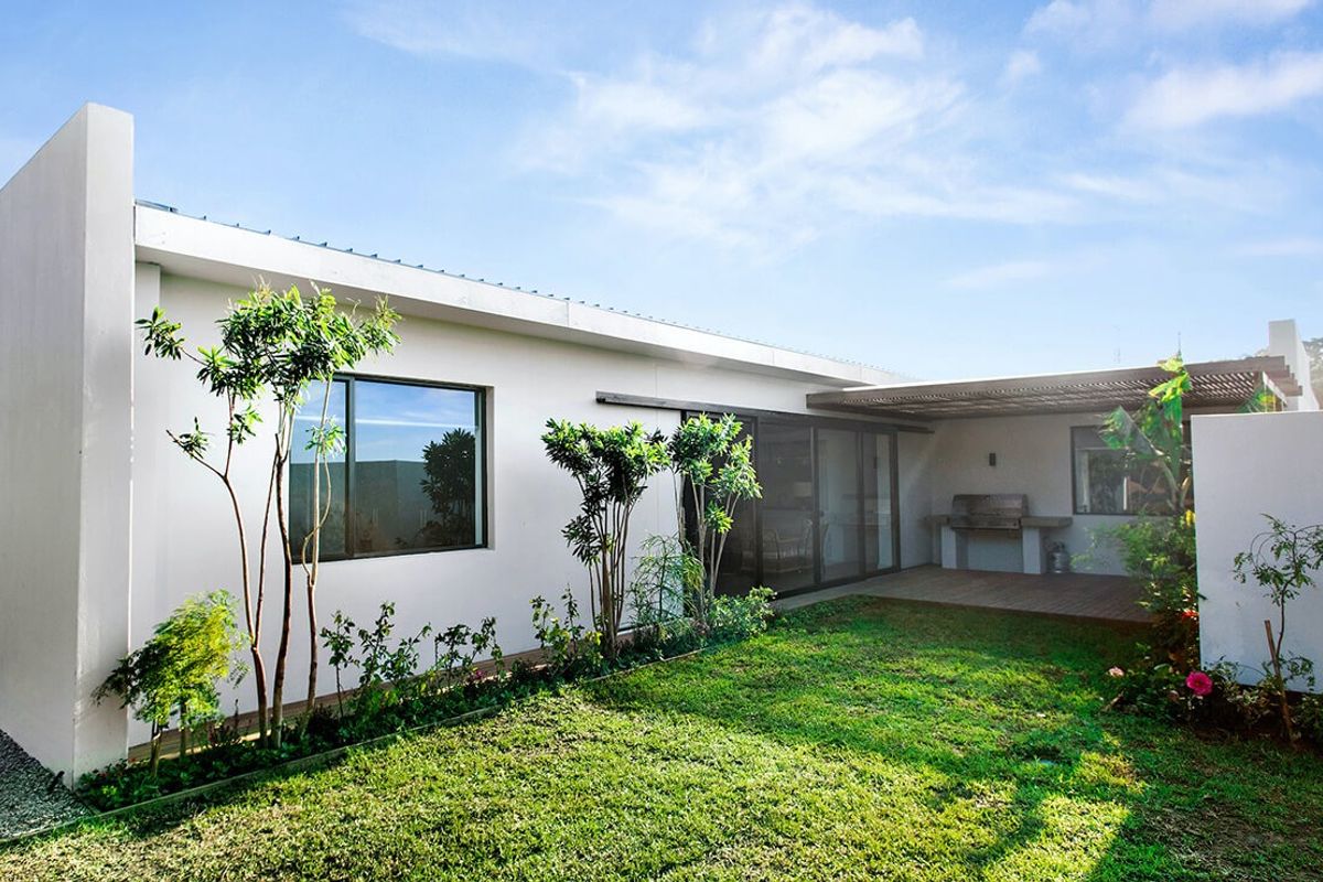 Rear view of the townhouse featuring a well-maintained garden, timber-decked covered patio, and a built-in braai area with sliding door access.