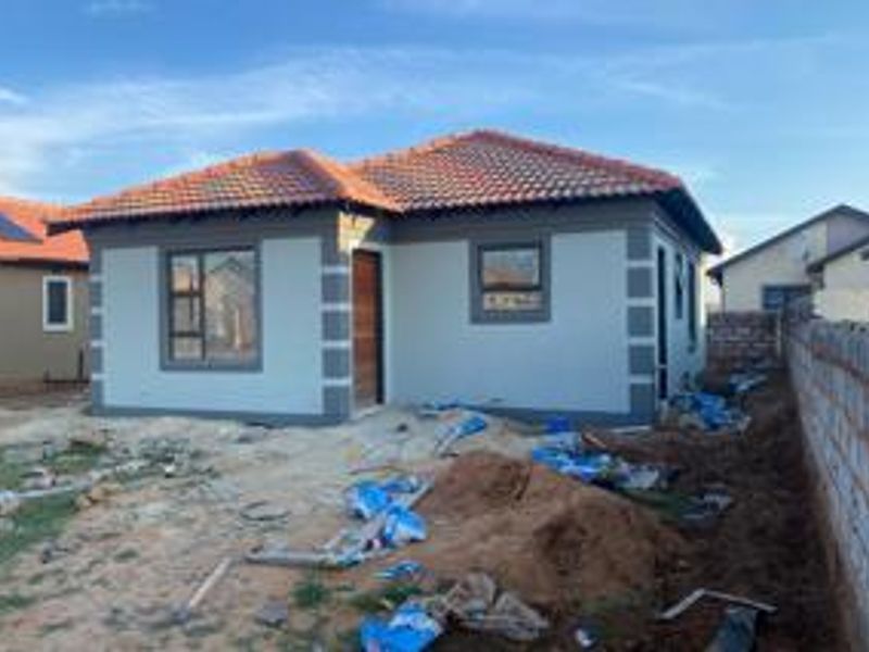 Front view of a newly constructed single-story house featuring a tiled roof, plastered exterior walls, and aluminium window frames, currently undergoing final site cleanup.