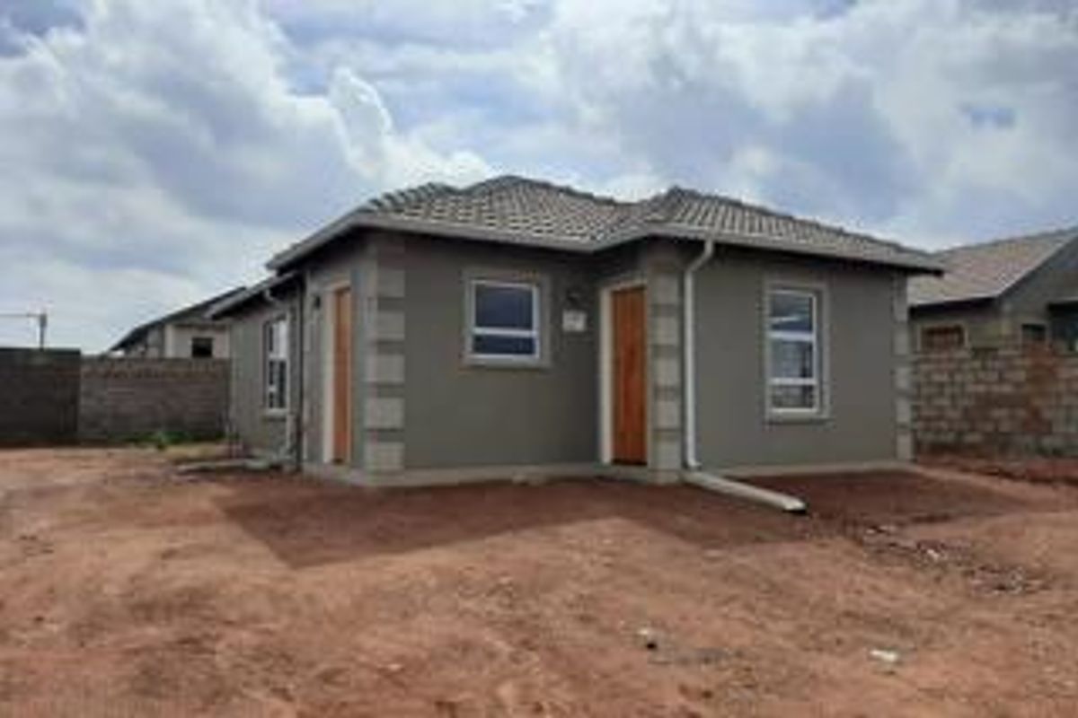 A modern single-story house exterior featuring a tiled roof, plastered walls, and aluminium window frames, set on an unlandscaped plot.