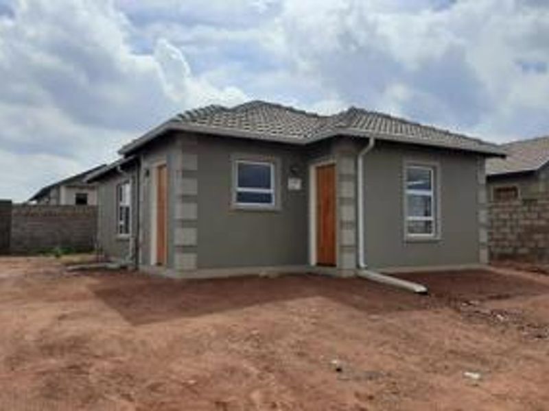A modern single-story house exterior featuring a tiled roof, plastered walls, and aluminium window frames, set on an unlandscaped plot.