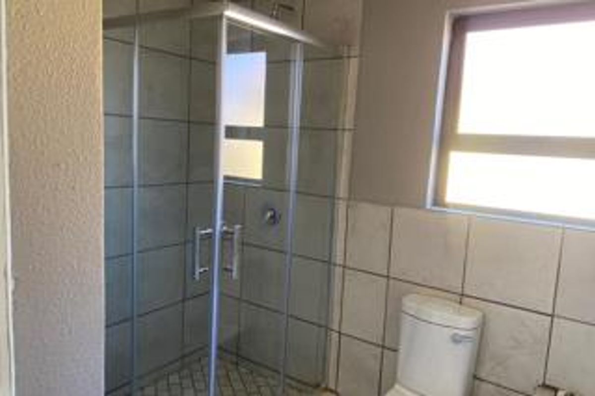 A functional bathroom featuring a glass-enclosed shower, a standard toilet, and tiled wall finishes with natural light from a window.