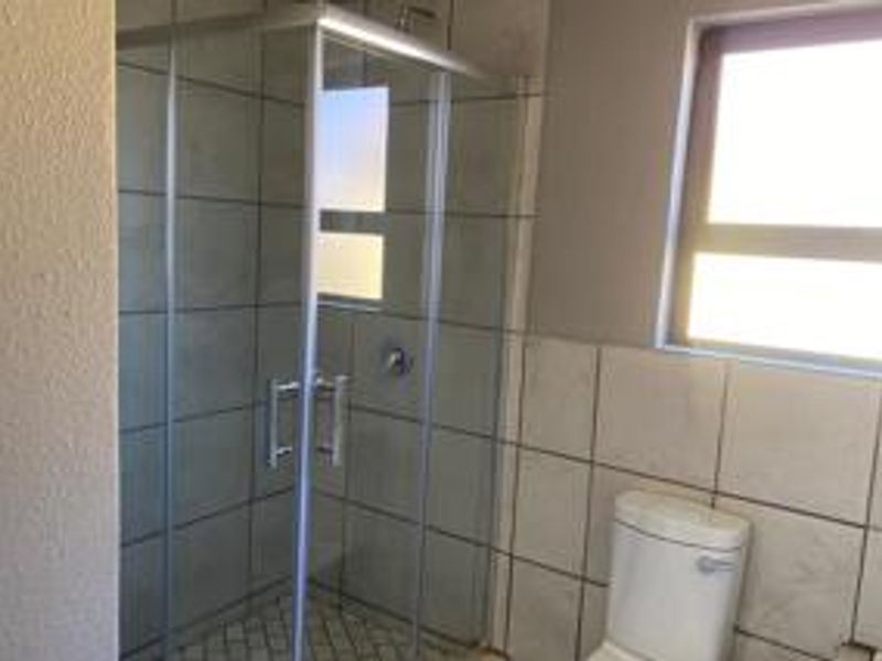 A functional bathroom featuring a glass-enclosed shower, a standard toilet, and tiled wall finishes with natural light from a window.