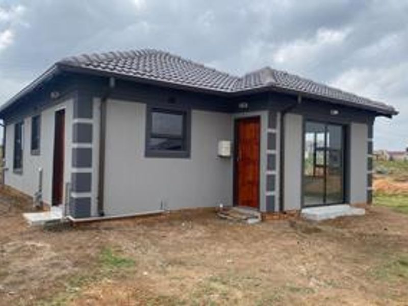 Rear view of a modern single-story house featuring a tiled roof, sliding glass doors, and a neutral grey exterior finish with contrasting corner detailing.