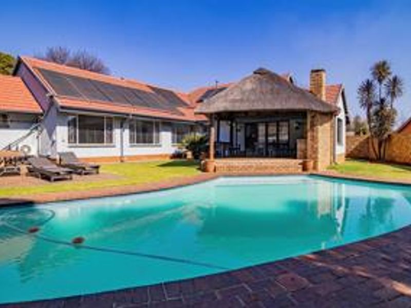 Spacious backyard featuring a swimming pool, a thatched lapa entertainment area, and solar heating panels installed on the roof.