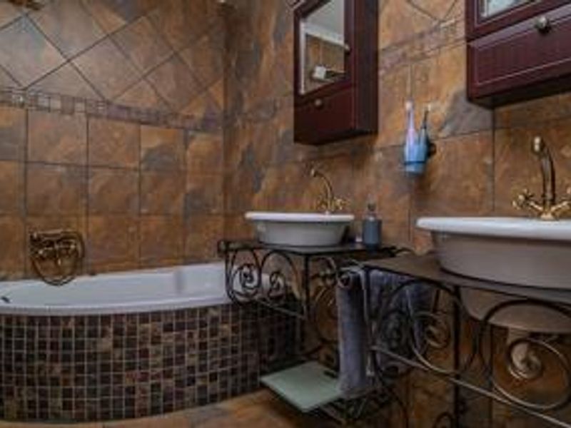 A bathroom featuring dual vessel sinks with brass fixtures, a built-in bathtub with mosaic tile surround, and wall-mounted cabinetry.
