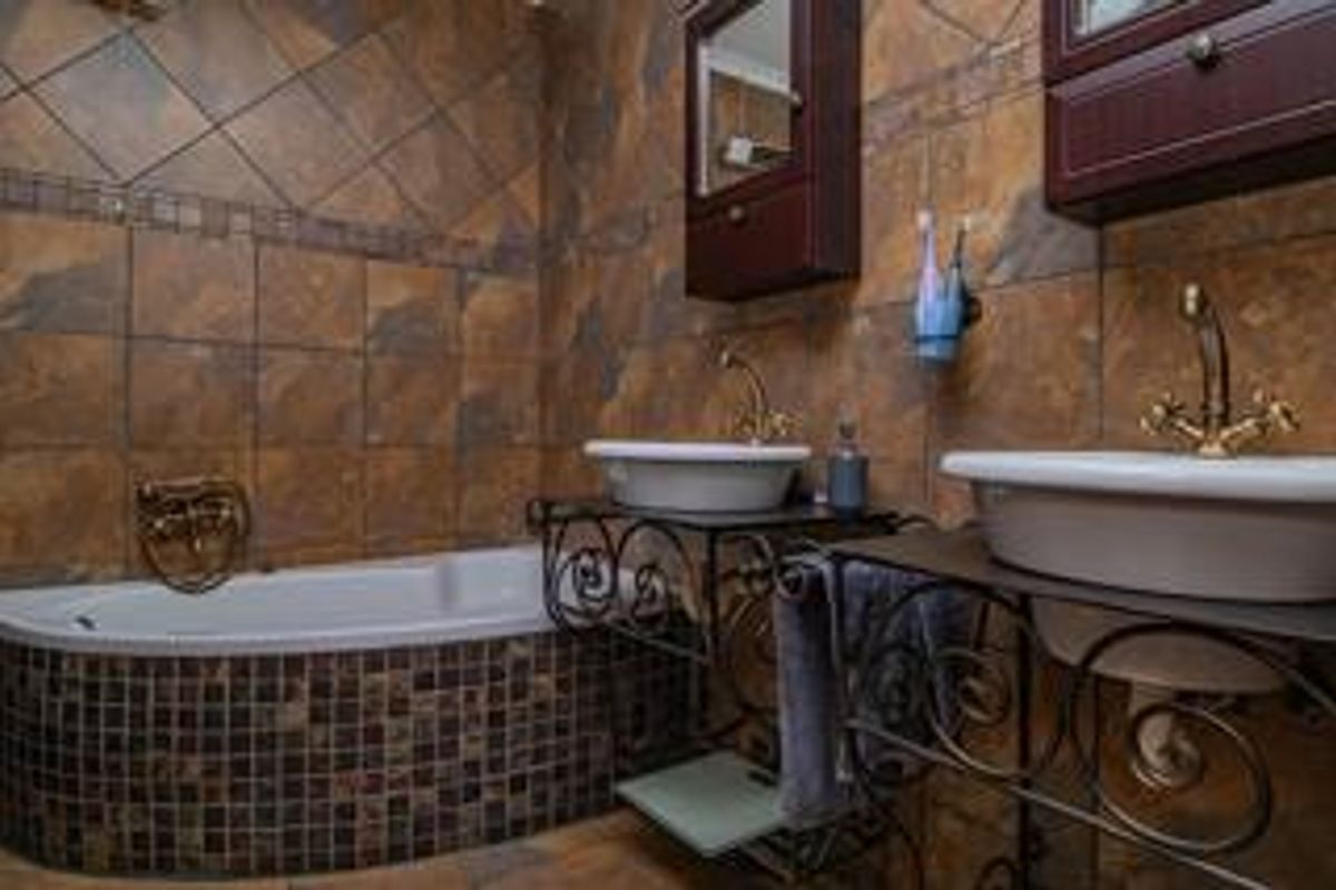 A bathroom featuring dual vessel sinks with brass fixtures, a built-in bathtub with mosaic tile surround, and wall-mounted cabinetry.