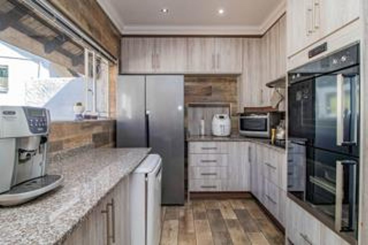 A modern kitchen featuring light wood-grain cabinetry, granite countertops, built-in double ovens, and tiled flooring with recessed lighting.